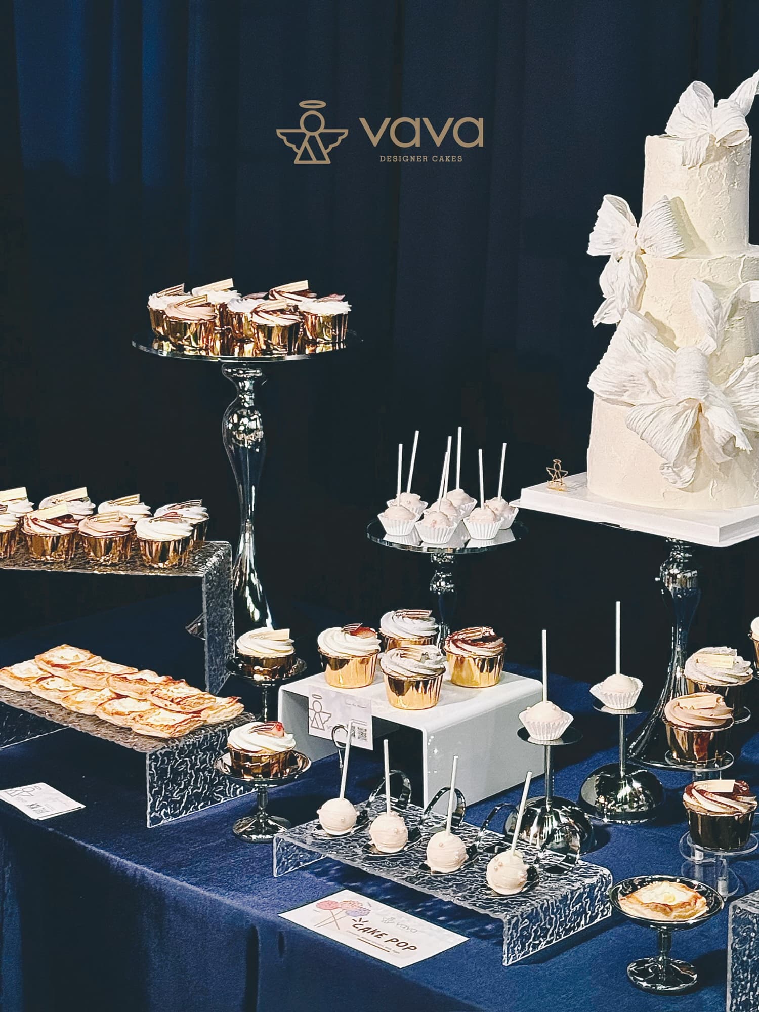 Elegant Vava dessert table in navy with a bow-draped white cake, cupcakes and cake pops