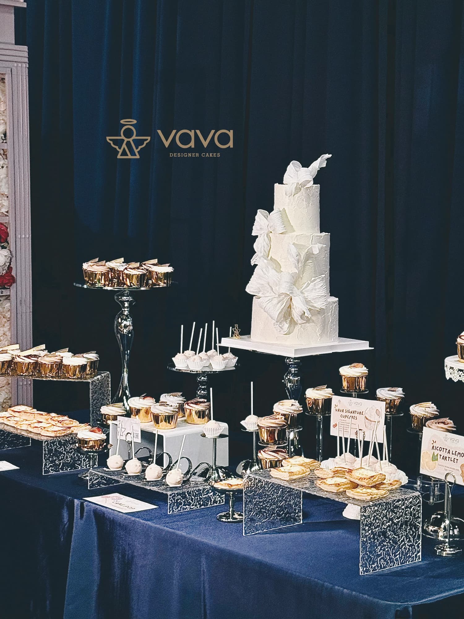 Navy velvet dessert table in Toronto with tiered white cake, gold cupcakes and pastries