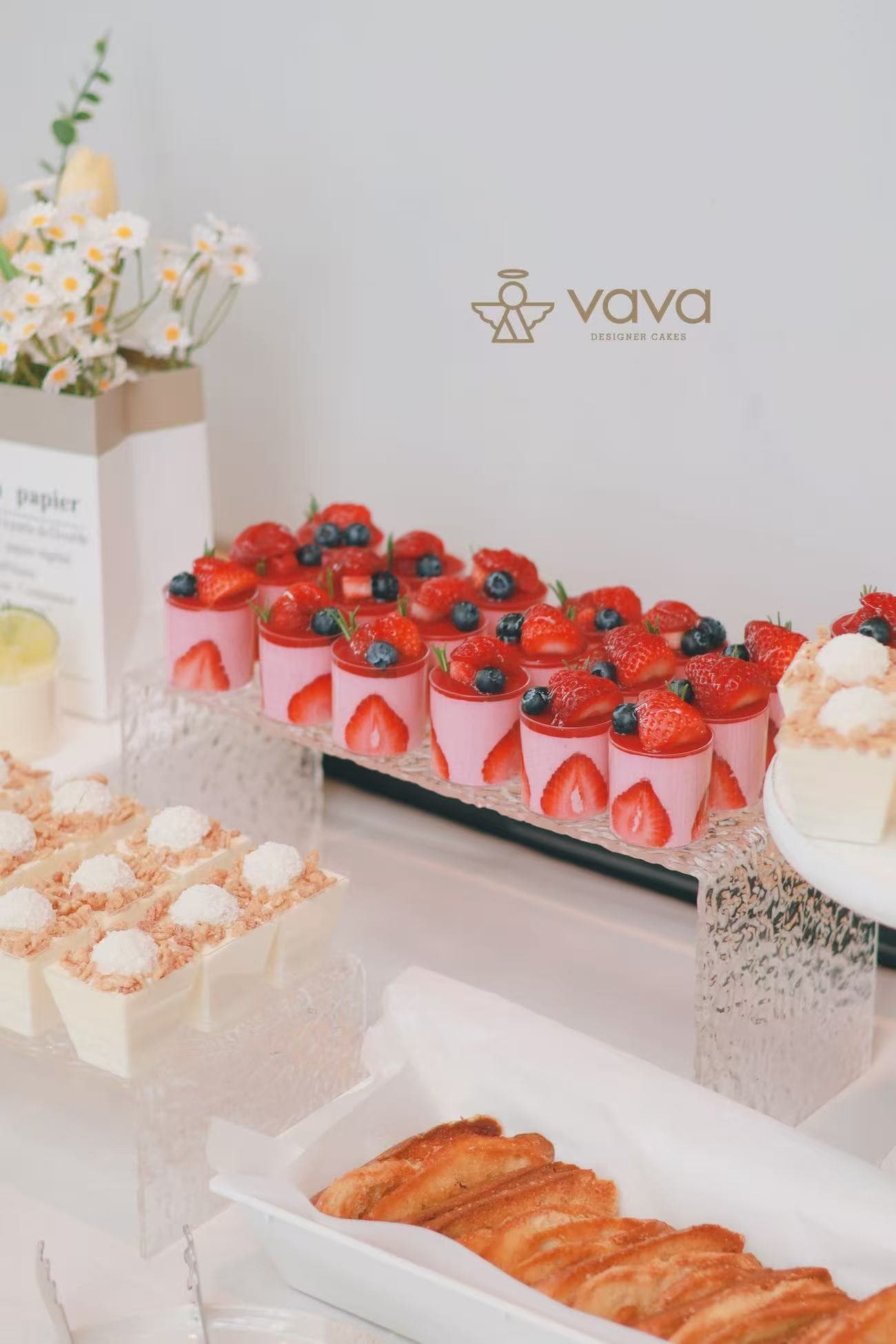 Strawberry mousse cups topped with fresh berries beside coconut cream desserts on a Vava sweet table